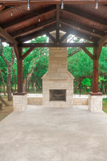 White stone fireplace built in to a covered patio. Trees can be seen in the background.