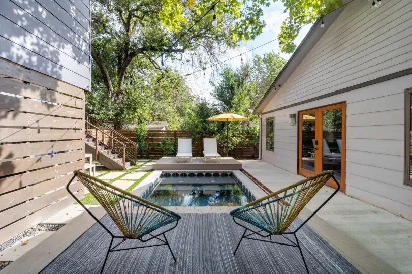 Two chairs facing a pool in a backyard. You can see the back of the house in the background and a fence and trees