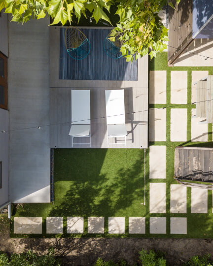 Birds eye view of a landscaped backyard. There is a pool, two white pool chairs, a patch of green grass, and white stone steps around the pool.