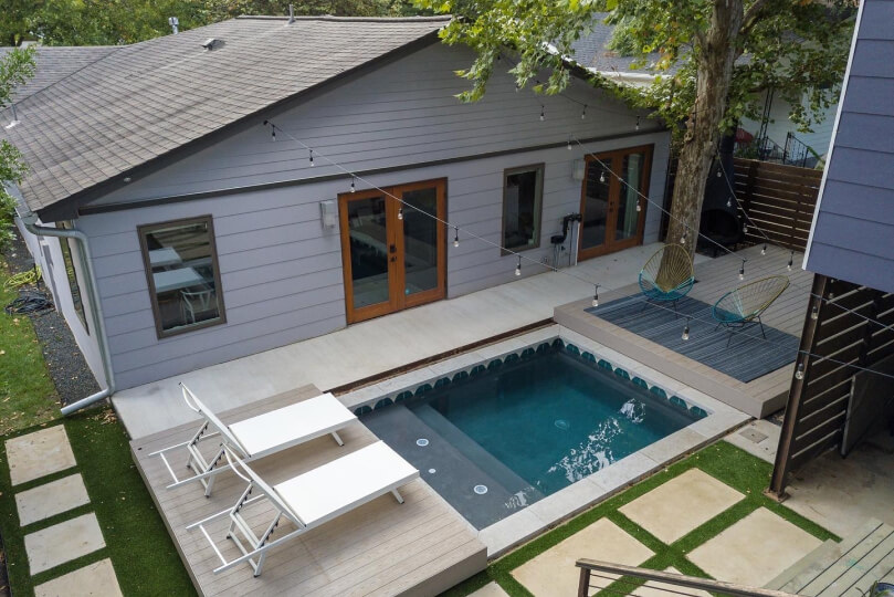 View of the back of a house with a pool, patio, and two white pool chairs