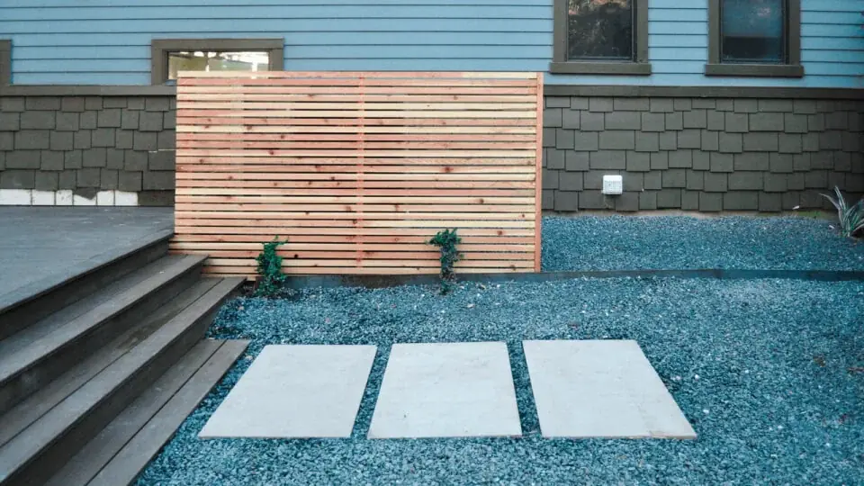 Steps to a deck leading down into a ock covered backyard. You can a wooden fence in the background.