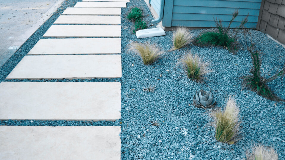 A pathway with white stone steps in a plant bed of rocks and small shrubs.