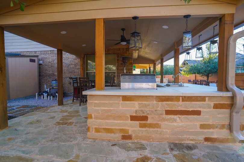 View of a light stone outdoor kitchen showing pendant lights hanging over the kitchen countertop.