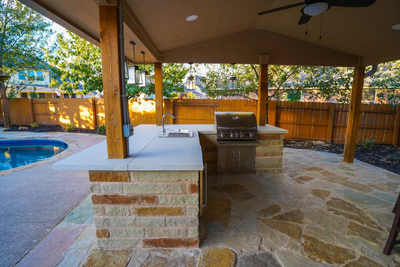 Light stone outdoor kitchen with a stainless steel grill and a sink.