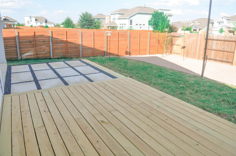 a wooden deck in a backyard. You can see grass, a tree, and a wooden fence in the background.