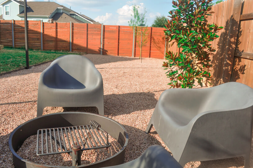 Close up of an outdoor fire pit with two chairs next to it.