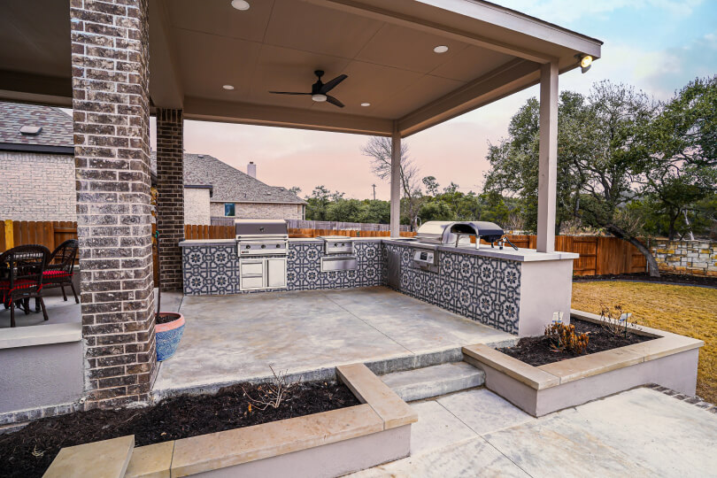 View of an outdoor kitchen built into a patio. You can also see two plant beds surrounding the patio.