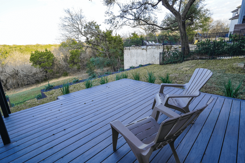 A backyard patio with two chairs on it. You can see grass and trees in the background.