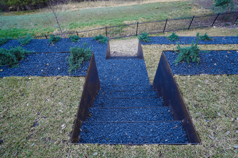 View of a backyard on a hill. There is grass and a fence in the background