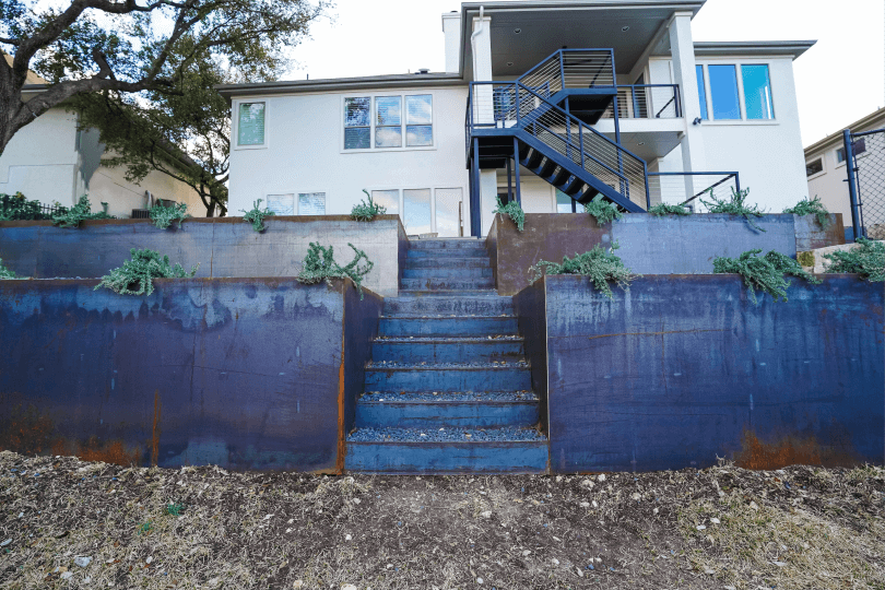 Bottom view of a backyard. There are stairs leading up to the house