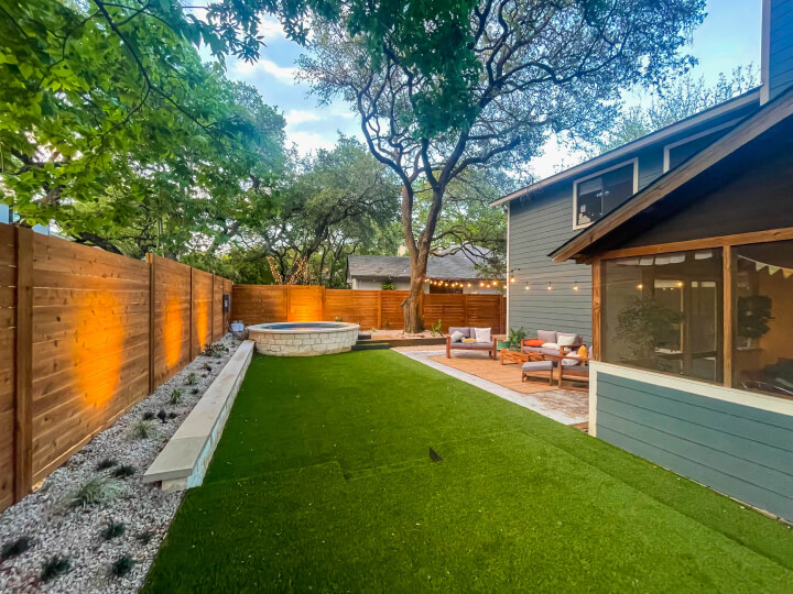 Side view of a backyard with green grass and a wooden fence surrounding it.