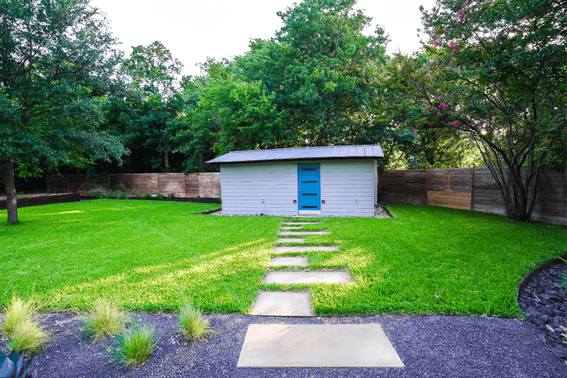 Backyard with green grass with a shed in the background.