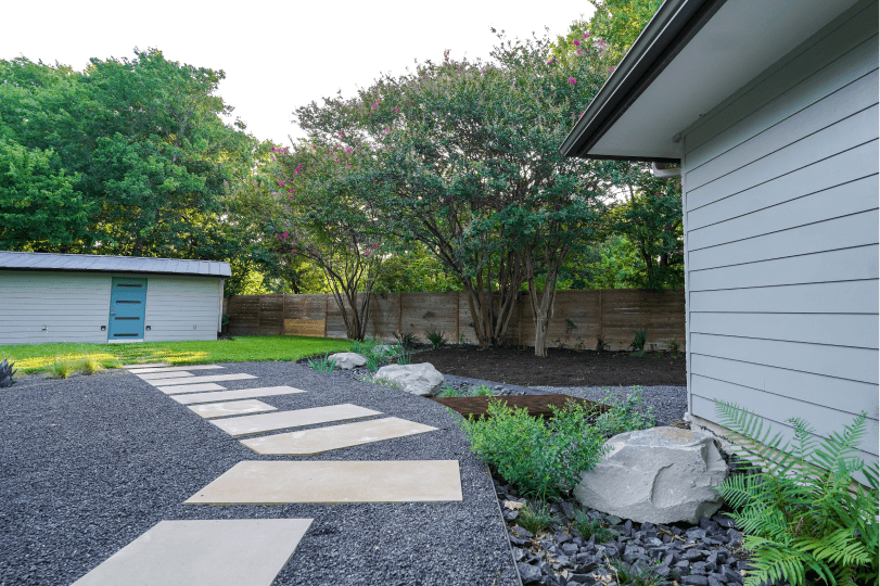 Landscaped backyard with black gravel, there is white stone steps.