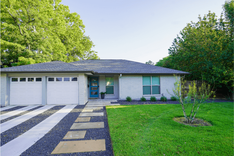 Front view of a landscaped front yard. There is black gravel on the left and green grass on the right.