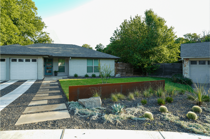 Front view of a landscaped front yard. There is green grass and a flower bed.