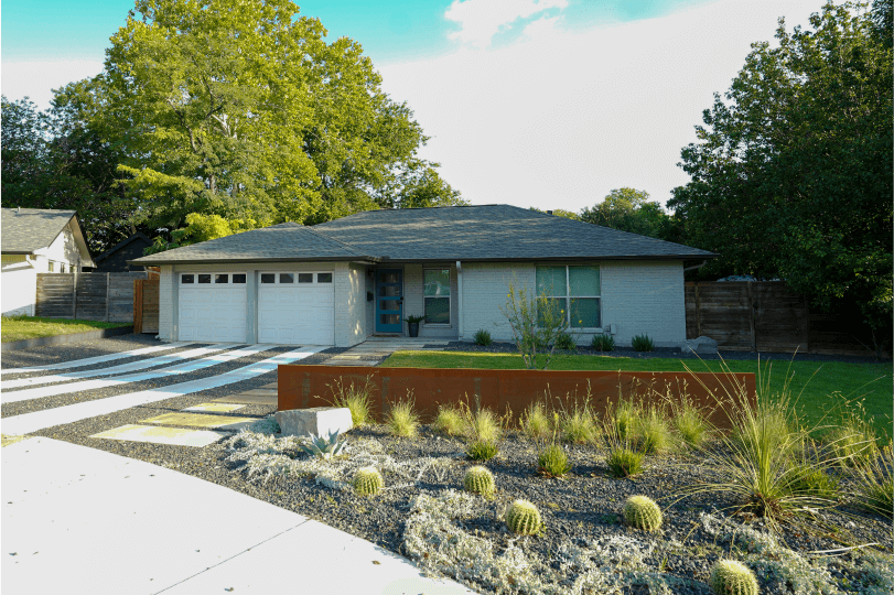 Side view of a landscaped front yard. There is green grass and a flower bed.
