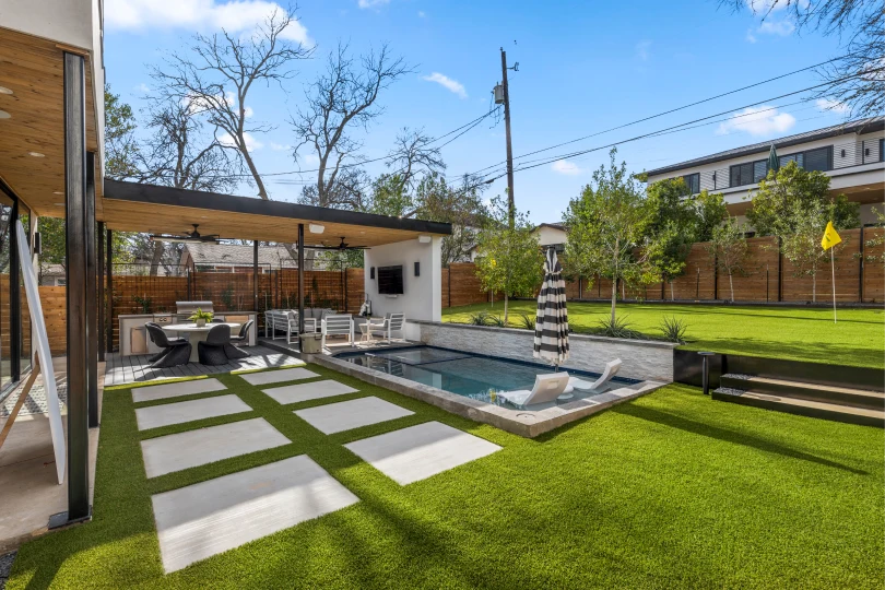 Backyard in Rosedale with stone pavers, an artificial turf putting green, and a covered patio with an outdoor kitchen.