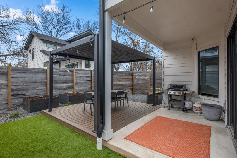The back porch of a home in Waller Creek with a concrete and wooden patio, a wooden pergola, and a professional landscape design.