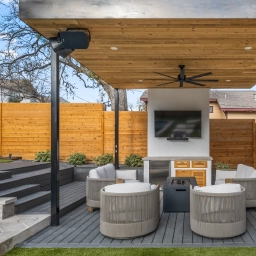 A backyard with a wooden pergola covering a fireplace and chairs.