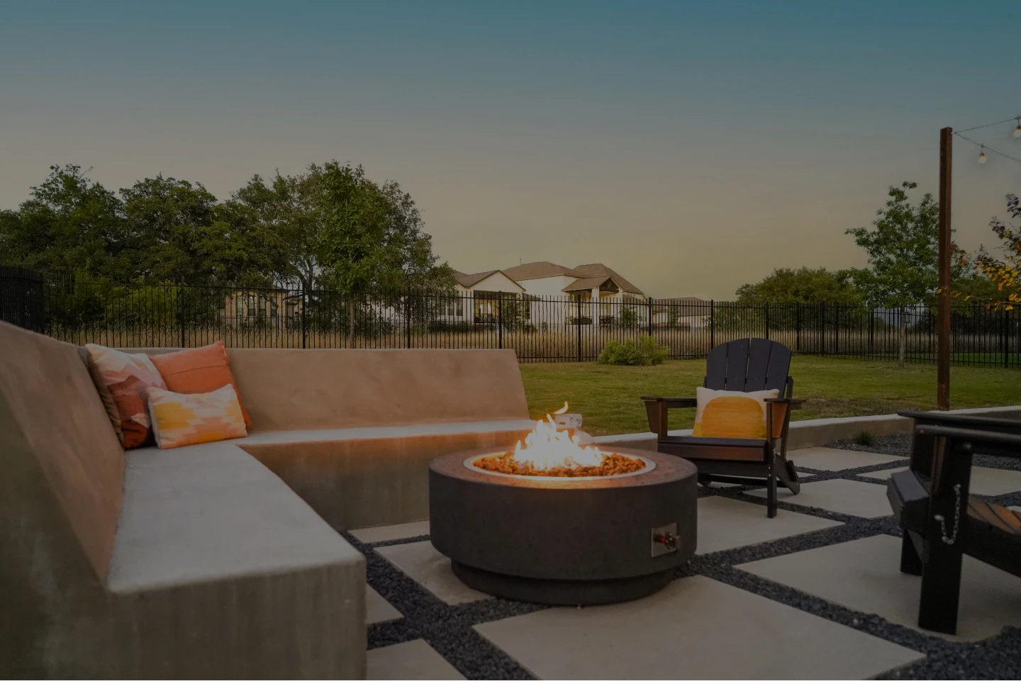 Outdoor chairs surrounding a rectangular fire pit with string lights hanging above.
