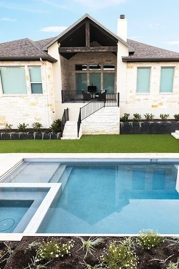 Cutters-Portfolio 5 Modern house with stone exterior, large windows, fenced backyard, and a rectangular in-ground pool with an attached hot tub.